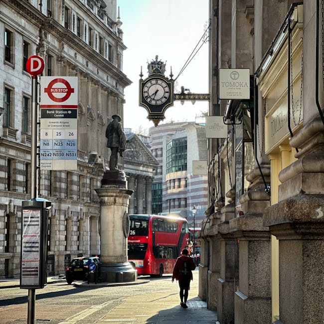 Close-up view of a street sign reading 'Square-Victoria' attached to a black pole in an urban setting. Behind the sign, tall modern glass office buildings reflect the surrounding cityscape, showcasing